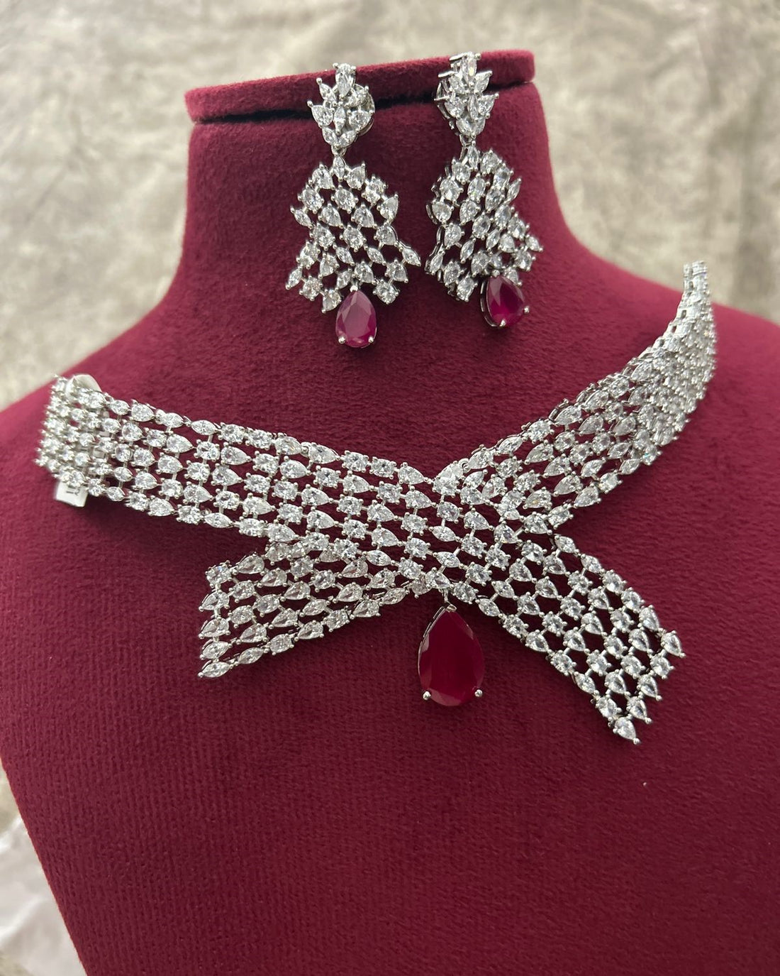 Silver necklace and earrings with red stones on a mannequin bust.