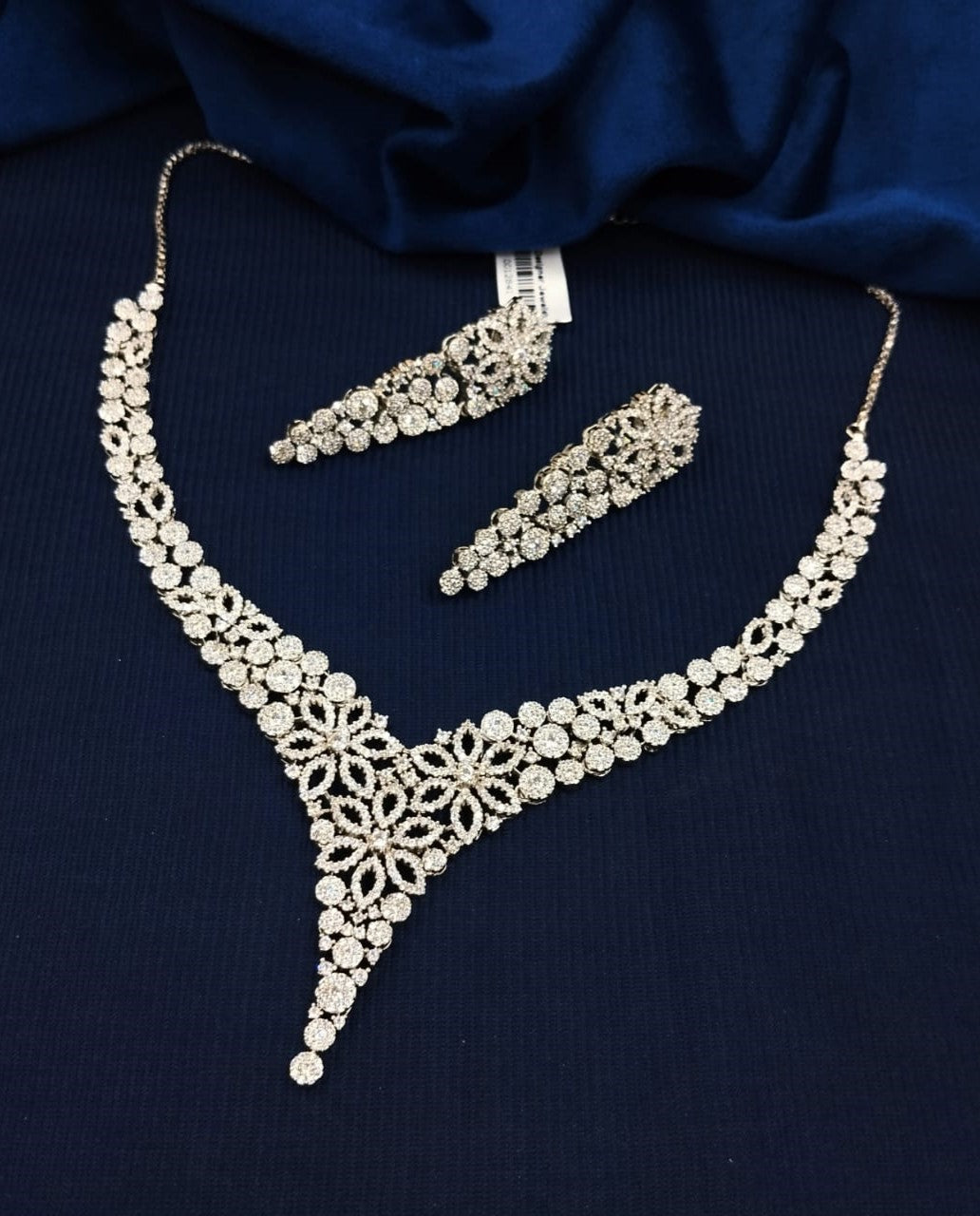 Silver necklace and earrings set on a dark blue fabric background