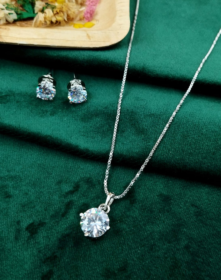 Silver necklace with a round pendant and matching earrings on a green fabric background.