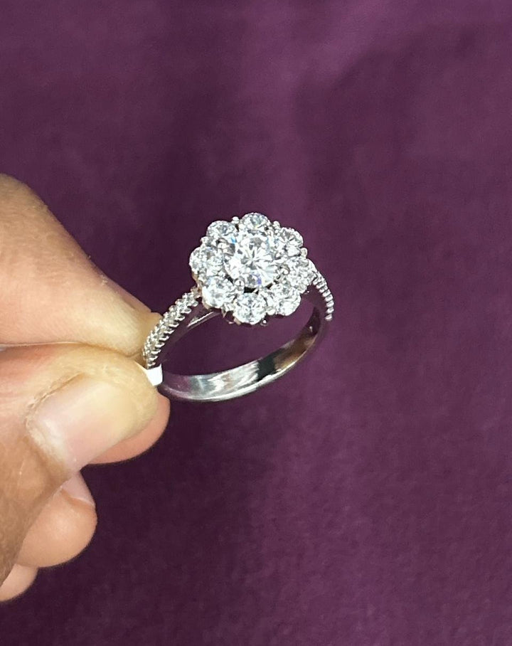 Silver ring with a diamond cluster held by a hand against a purple background