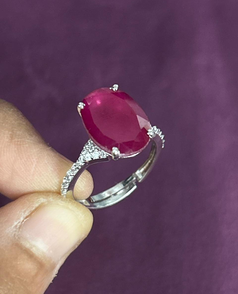 Silver ring with a red gemstone held by a hand against a purple background