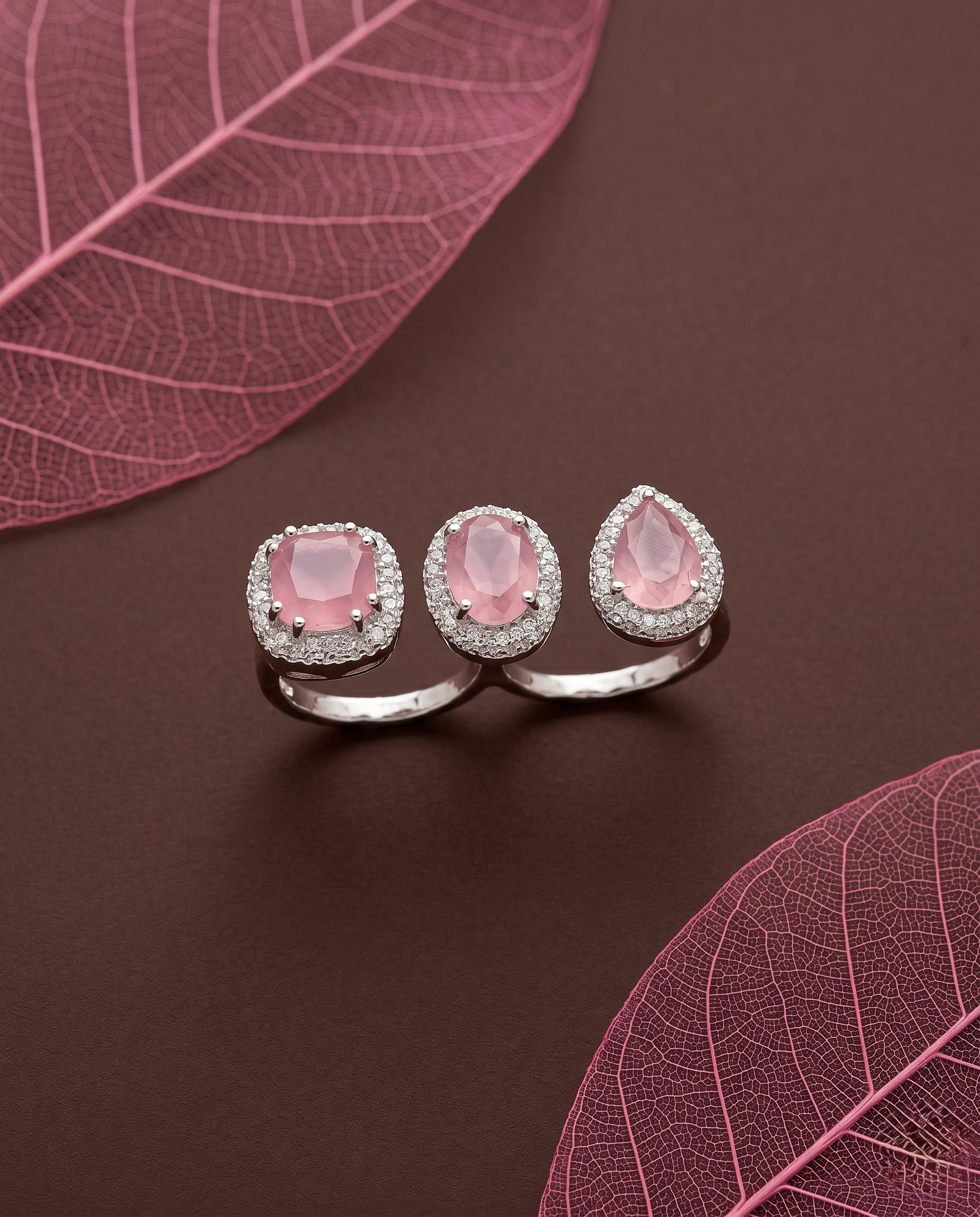 Silver ring with baby pink gemstones on a brown surface with pink leaves 

