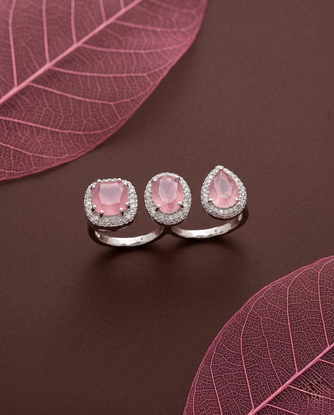 Silver ring with baby pink gemstones on a brown surface with pink leaves 

