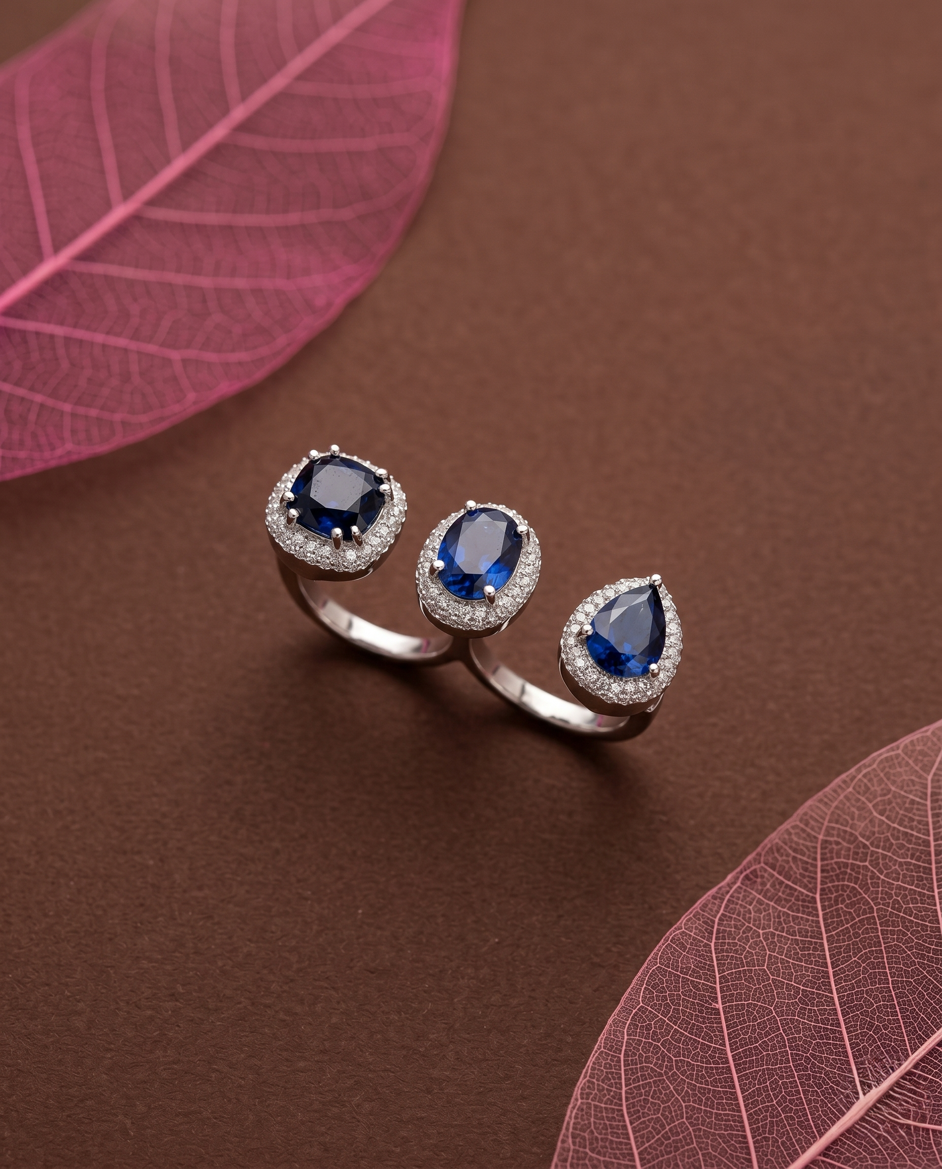 Silver ring with blue gemstones on a brown surface with pink leaves