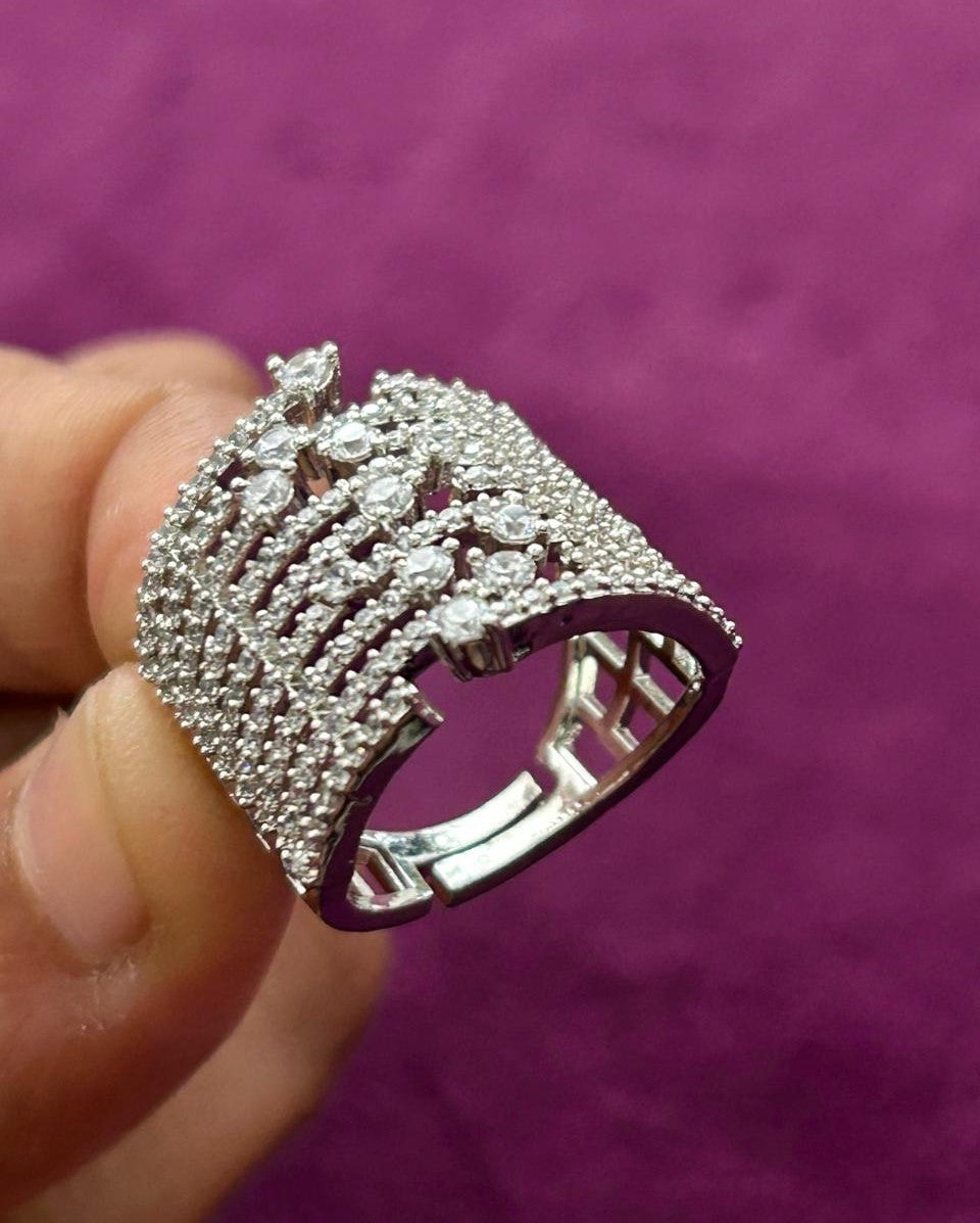 Silver ring with gemstones held by a hand against a purple background