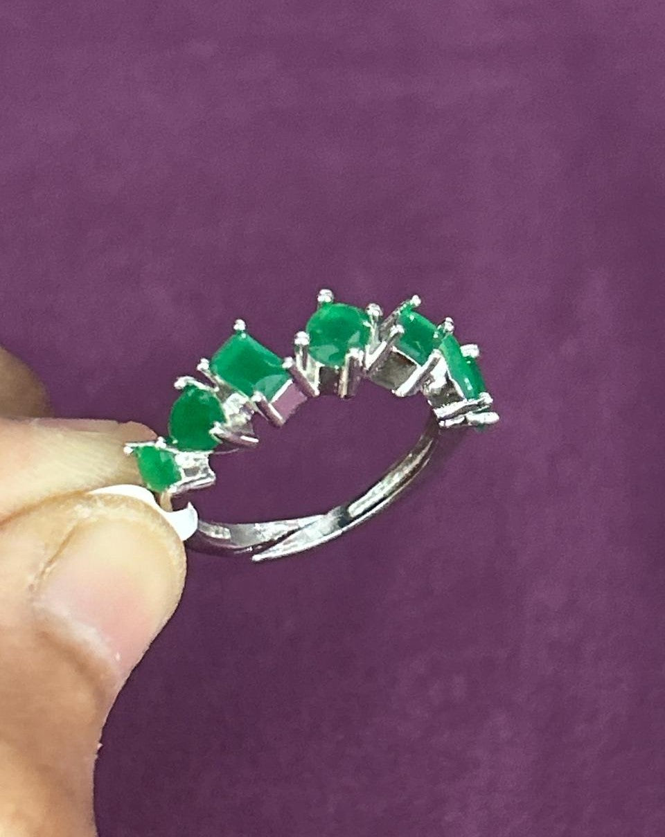 Silver ring with green gemstones held by a hand against a purple background
