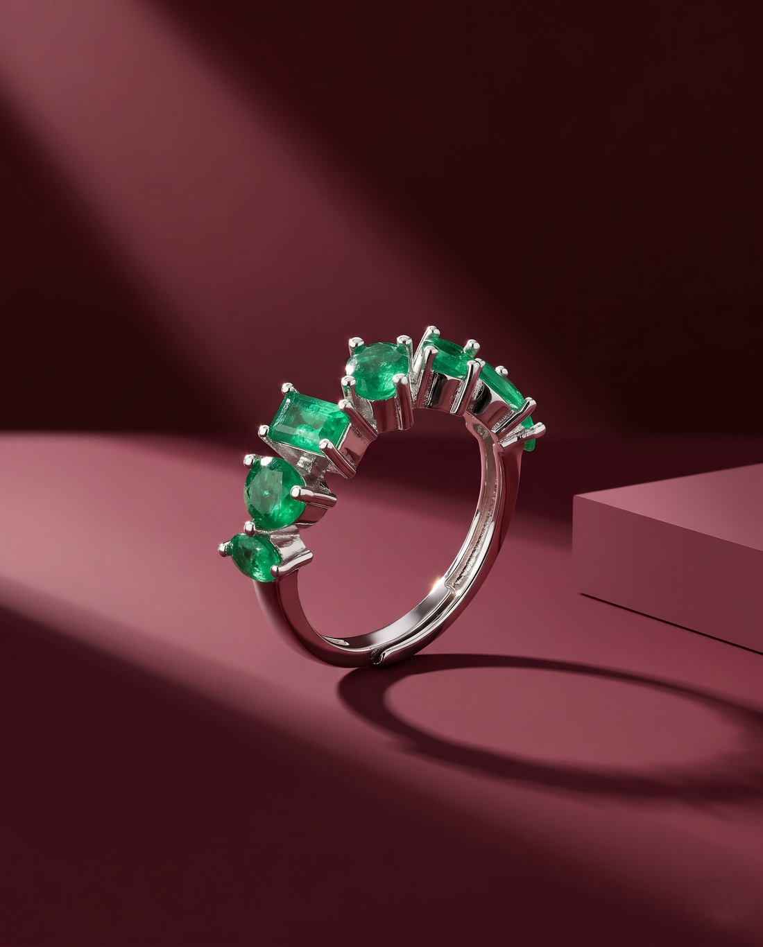 Silver ring with green gemstones on a maroon background