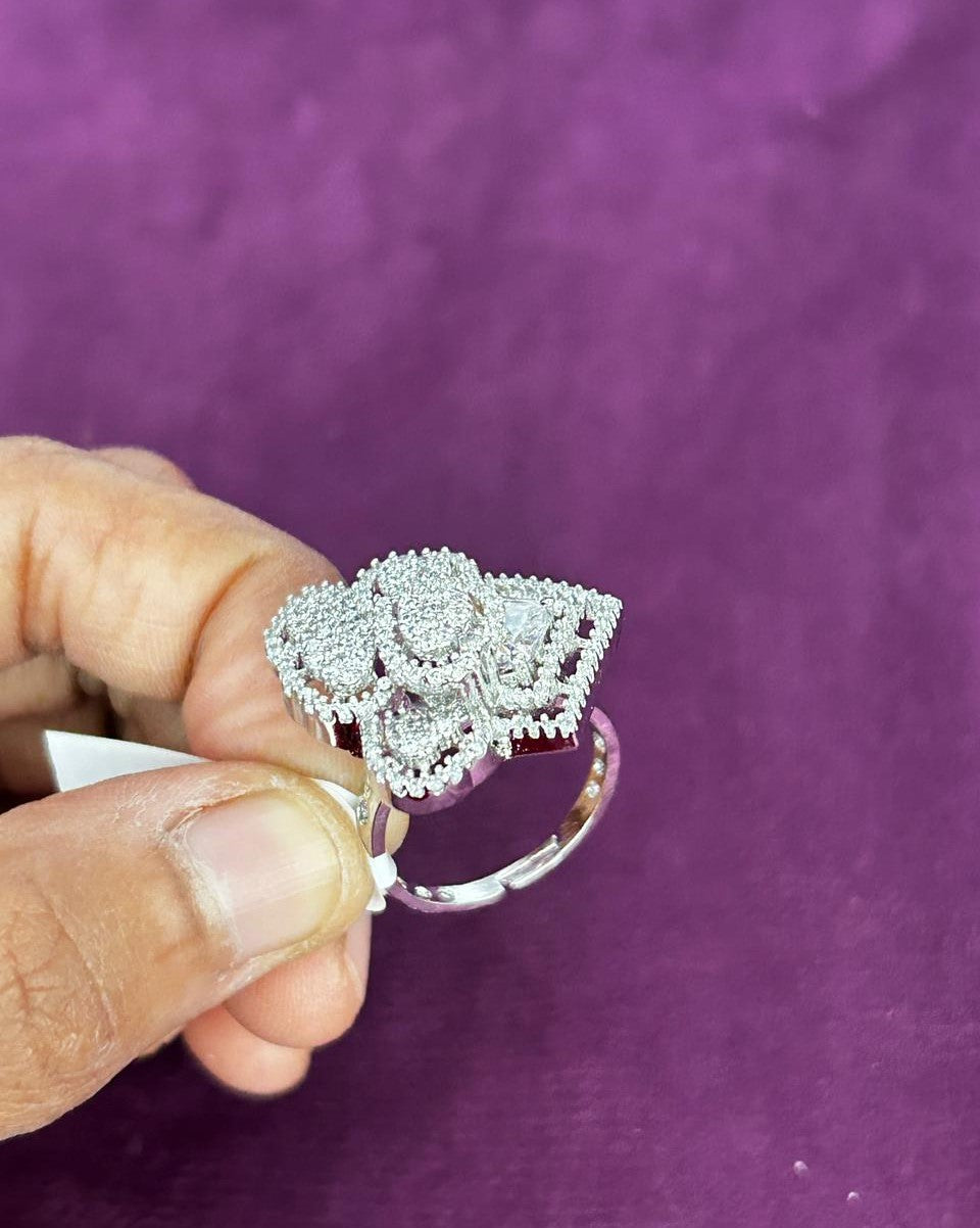 Silver ring with intricate design held by a hand against a purple background