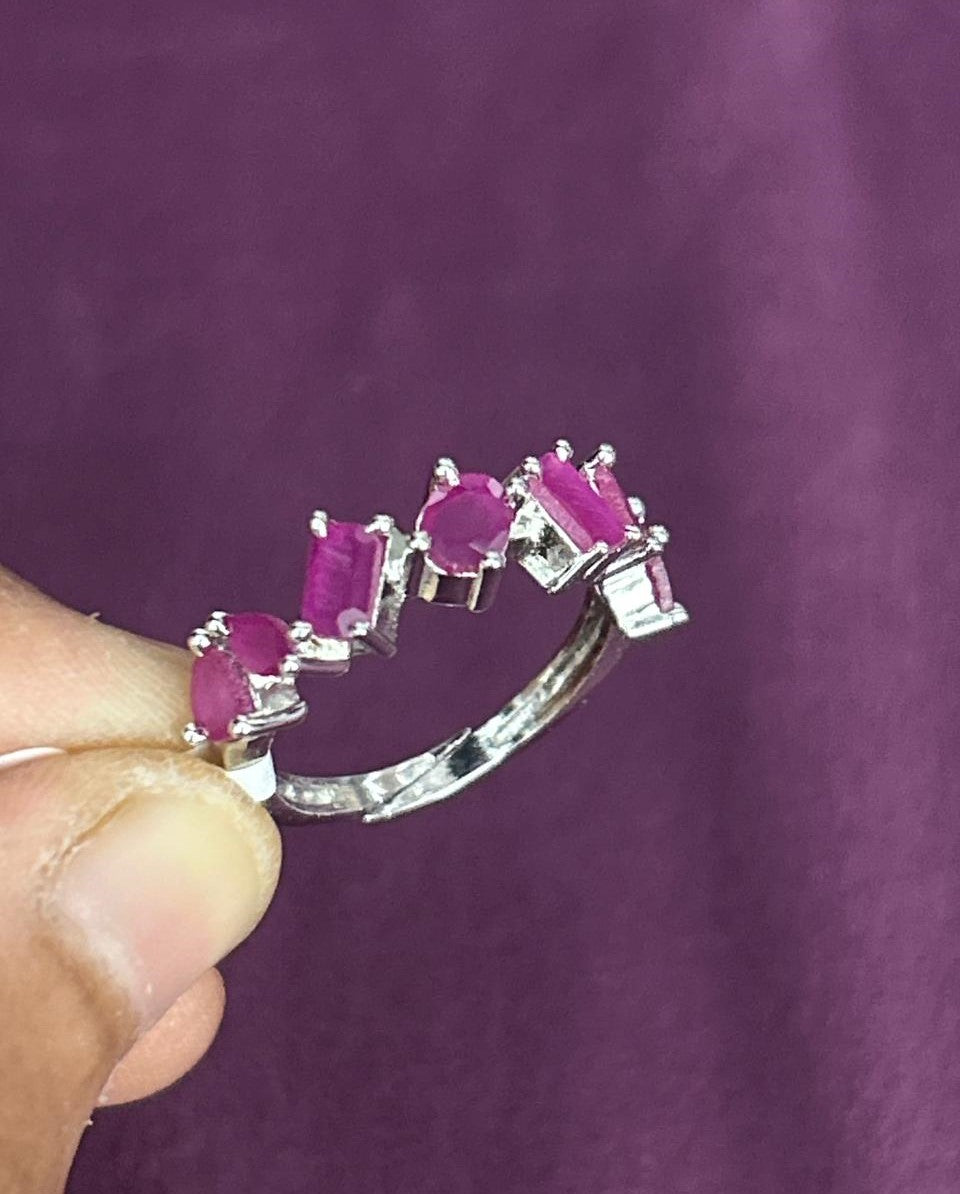 Silver ring with pink gemstones held against a purple background