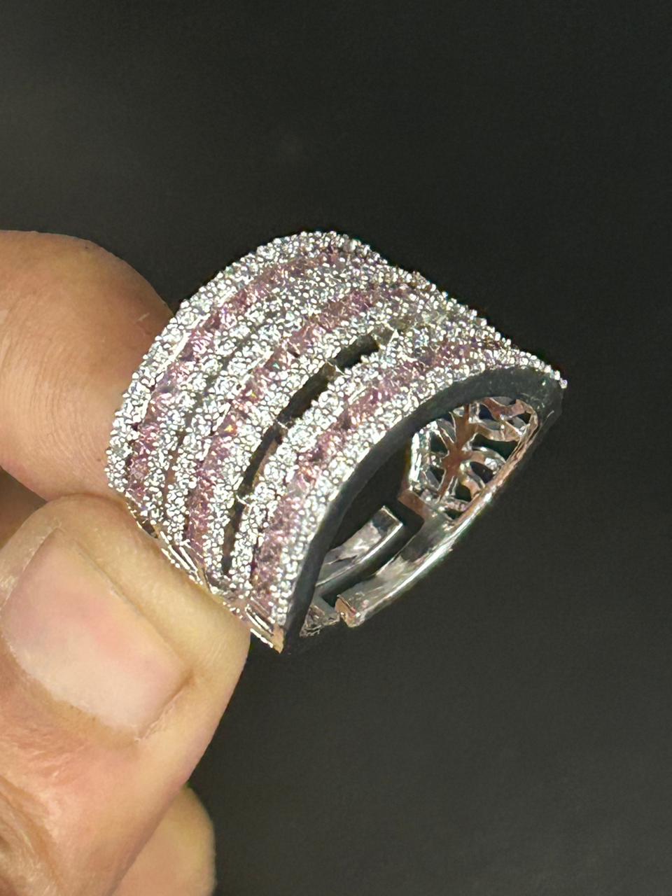 Silver ring with pink gemstones held by a finger against a dark background