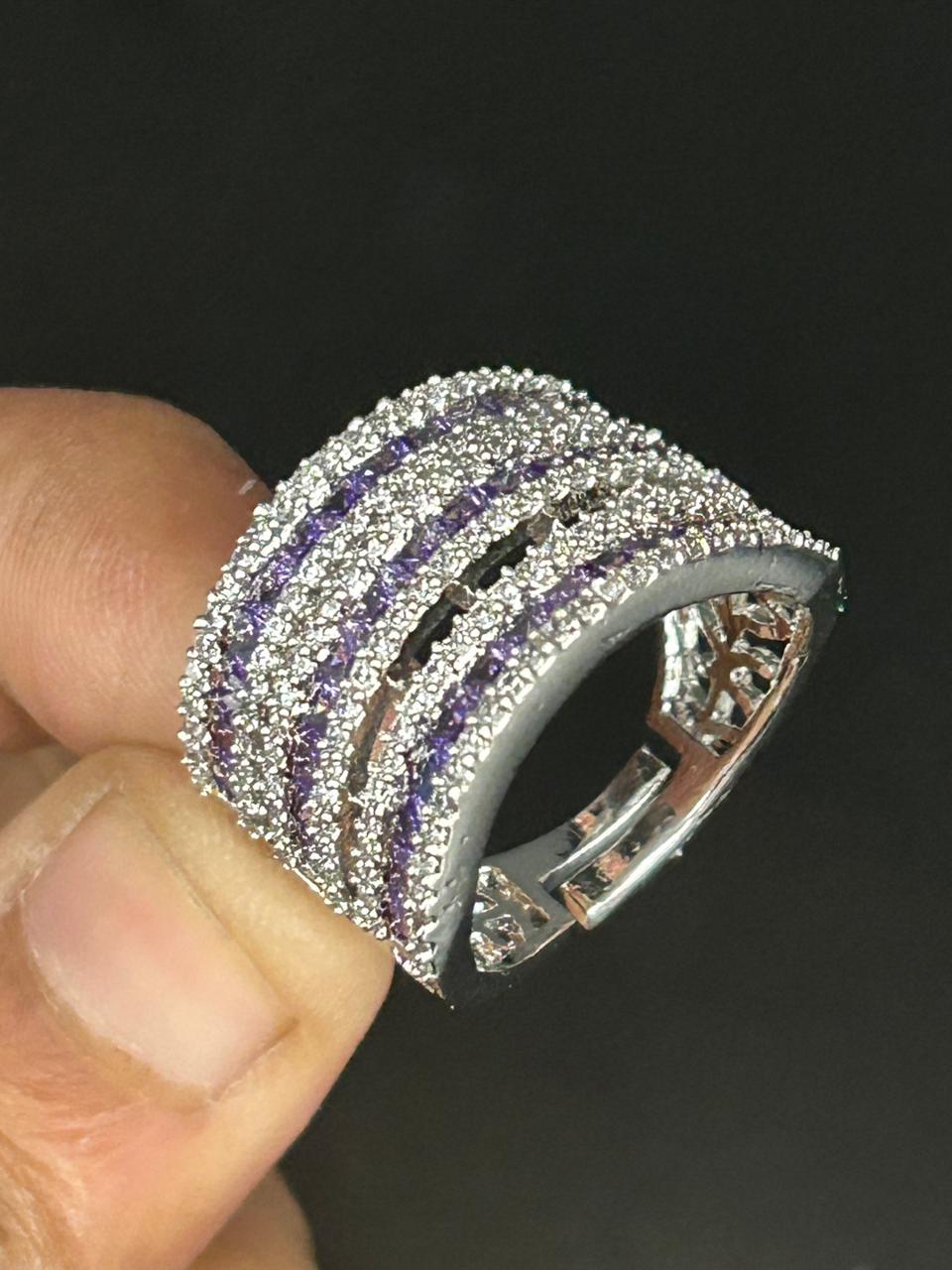 Silver ring with purple stones held by a hand against a dark background