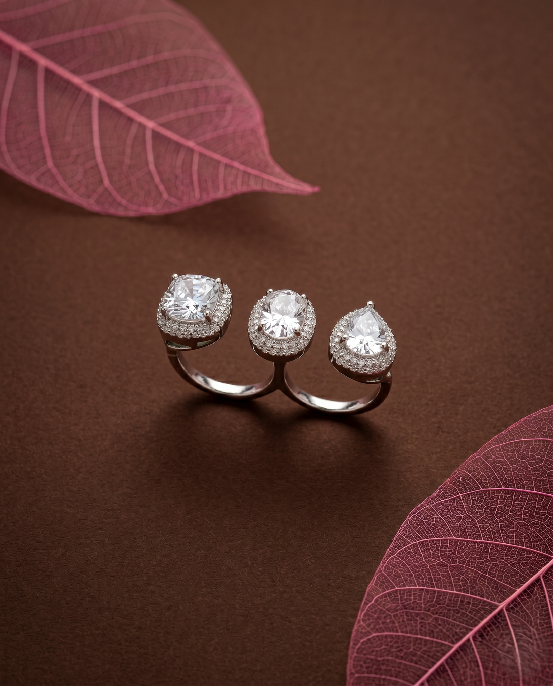 Silver ring with white gemstones on a brown surface with pink leaves 

