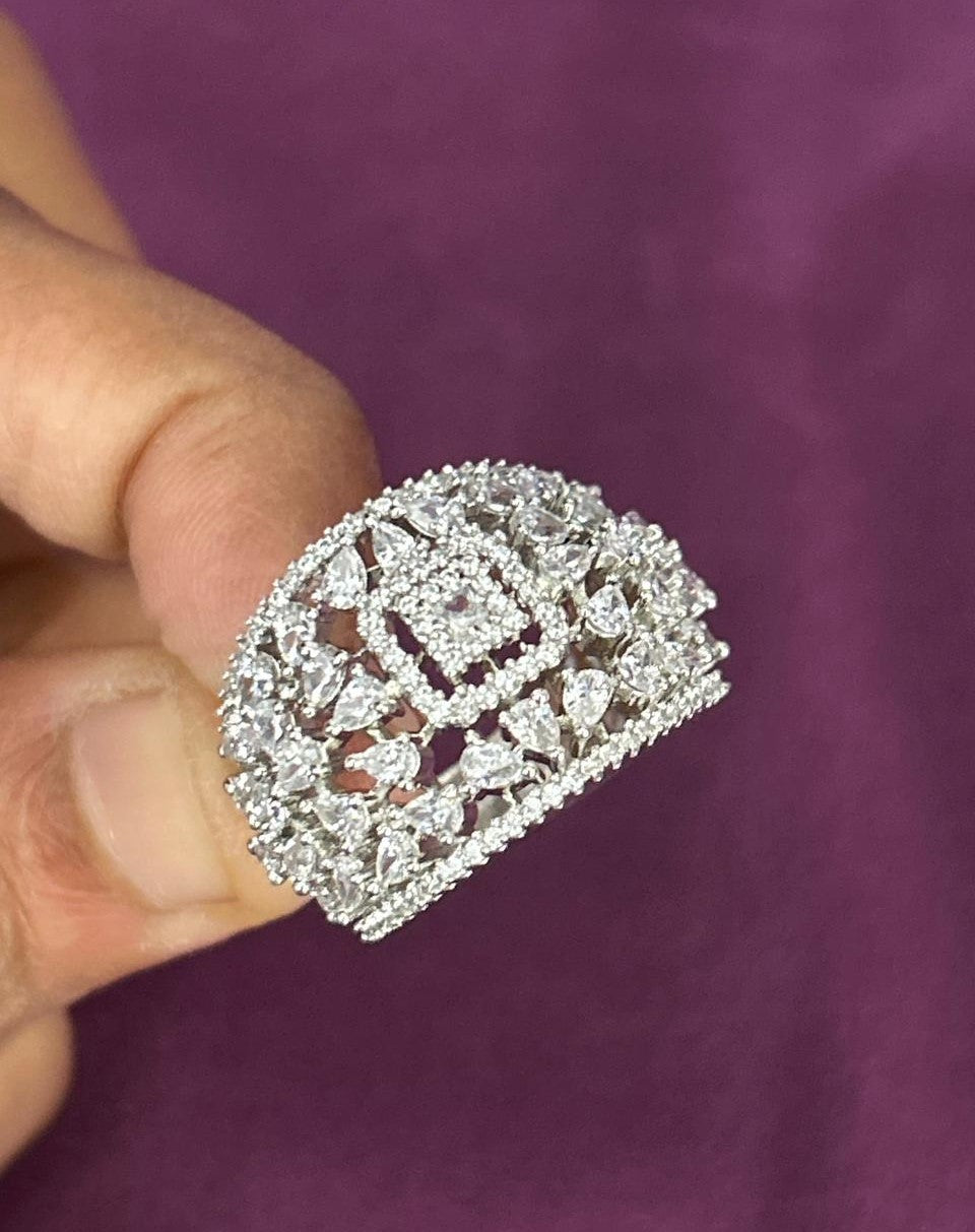 Silver ring with gemstones held by a hand against a purple background