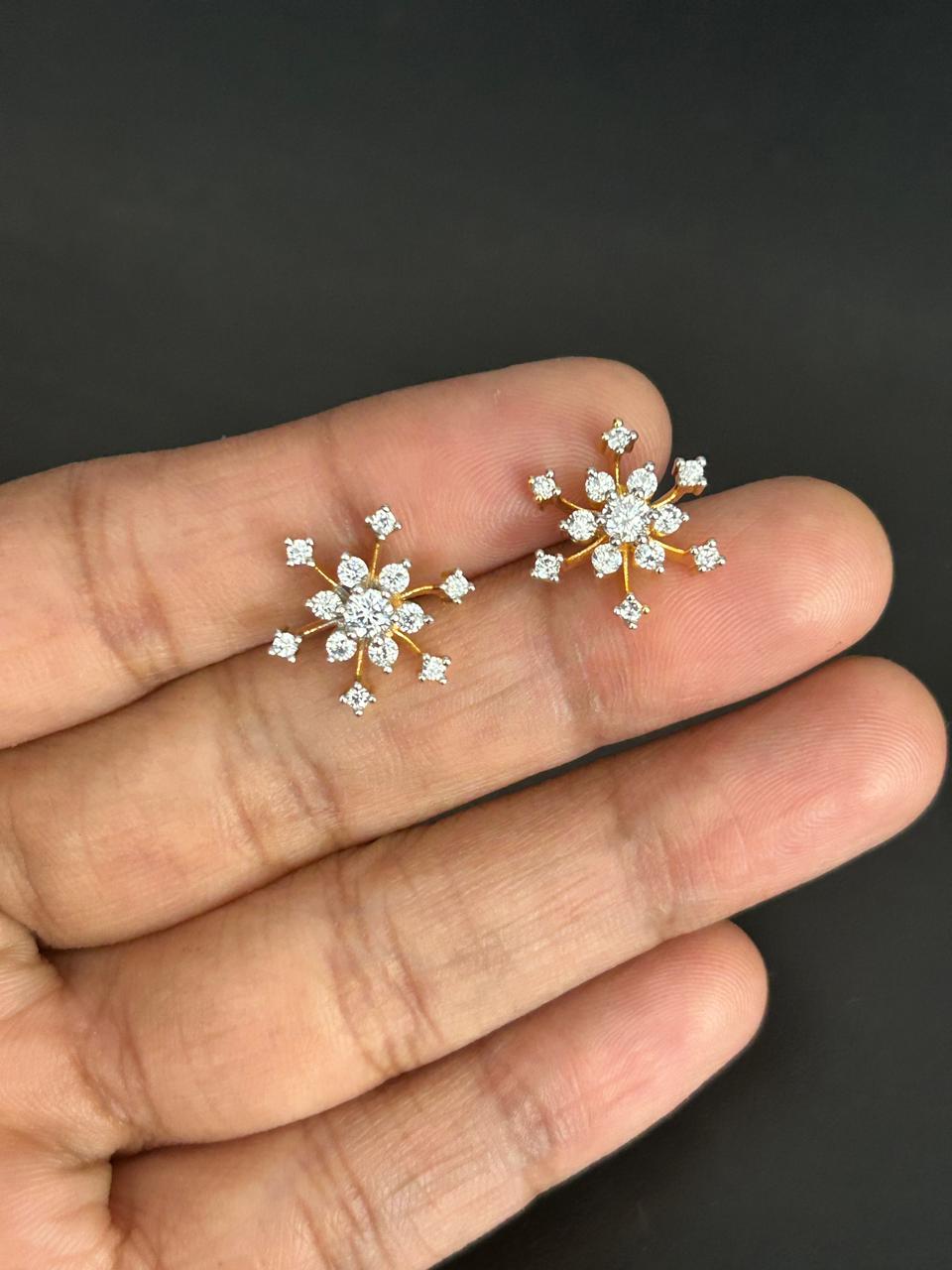 Snowflake-shaped earrings held between fingers against a dark background
