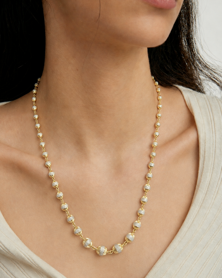 A close-up of a model wearing a delicate gold necklace with small white pearl-like beads and a central cluster of larger clear stones.