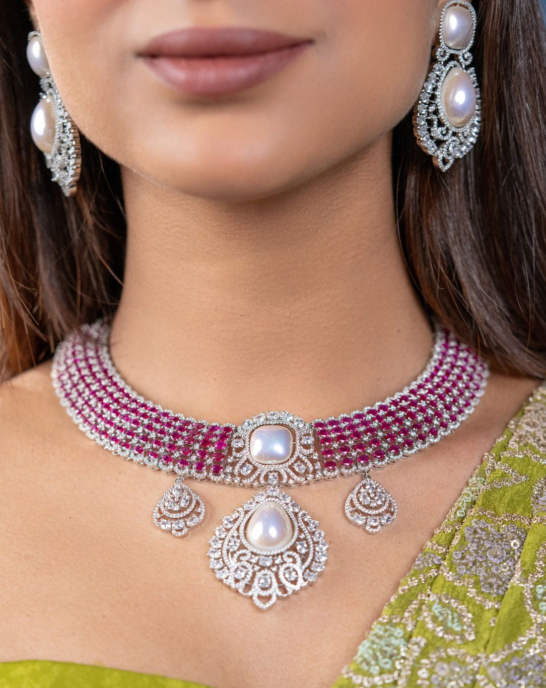 Close-up of a woman wearing a silver and red necklace with matching earrings, set against a blurred background.