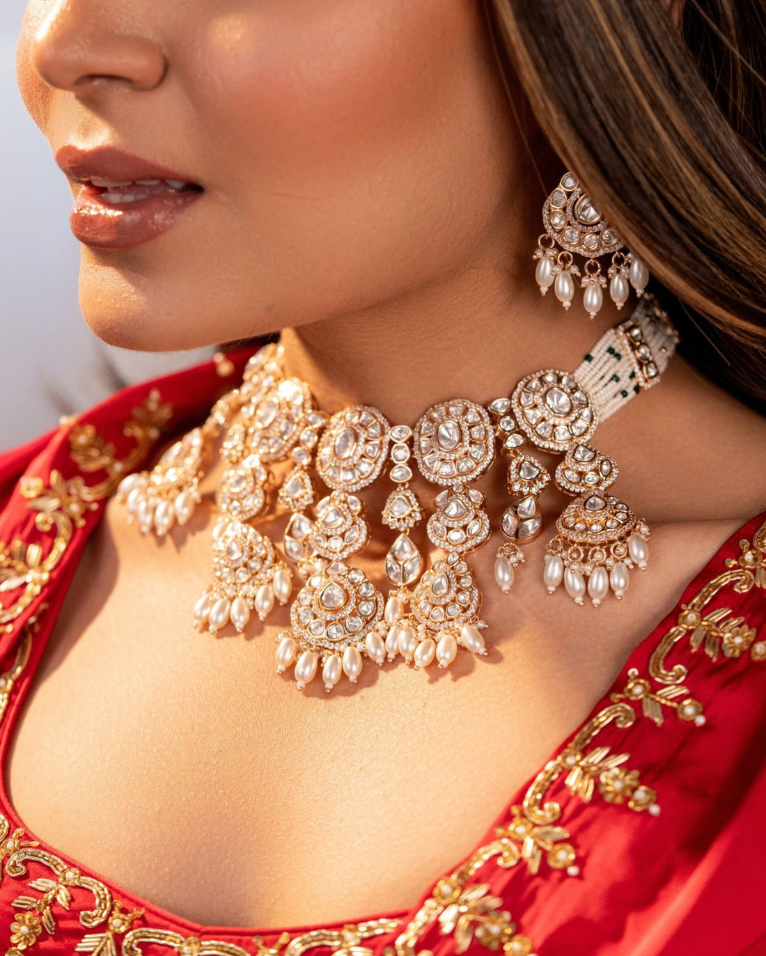 Close-up of a woman wearing a red saree with gold embroidery and a matching jewelry set.