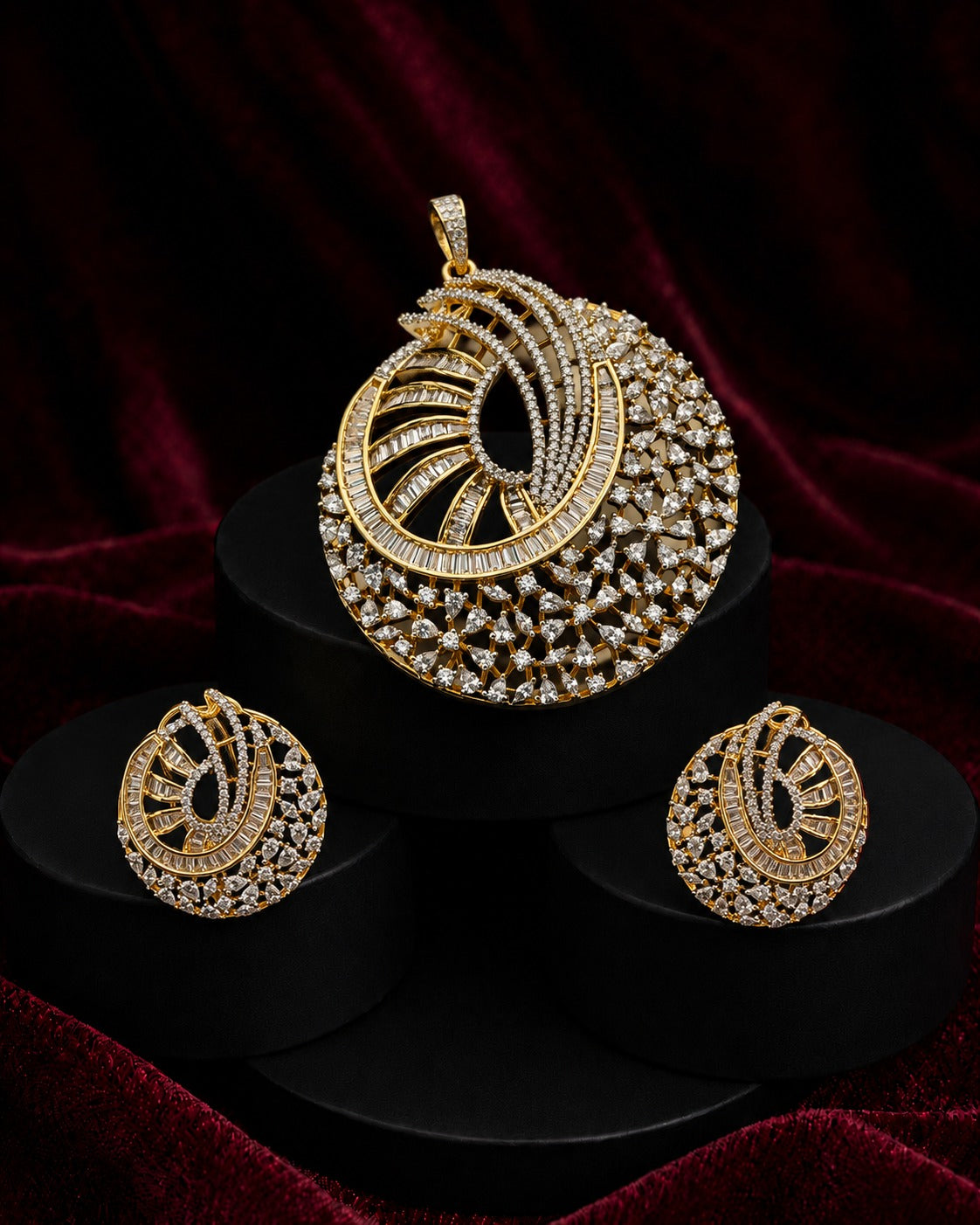 Gold-toned Indian ethnic jewelry set featuring a large pendant and two matching earrings, embellished with clear stones, displayed on black pedestals against a dark red velvet background.
