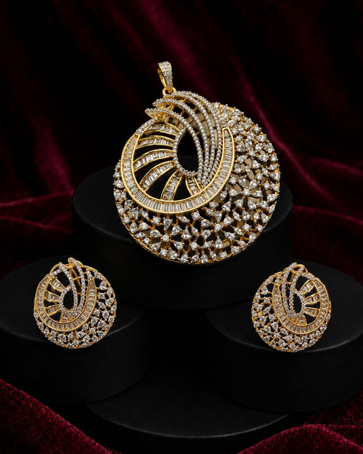 Gold-toned Indian ethnic jewelry set featuring a large pendant and two matching earrings, embellished with clear stones, displayed on black pedestals against a dark red velvet background.