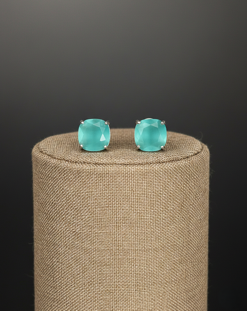 Turquoise stud earrings on a beige cushion with a dark background