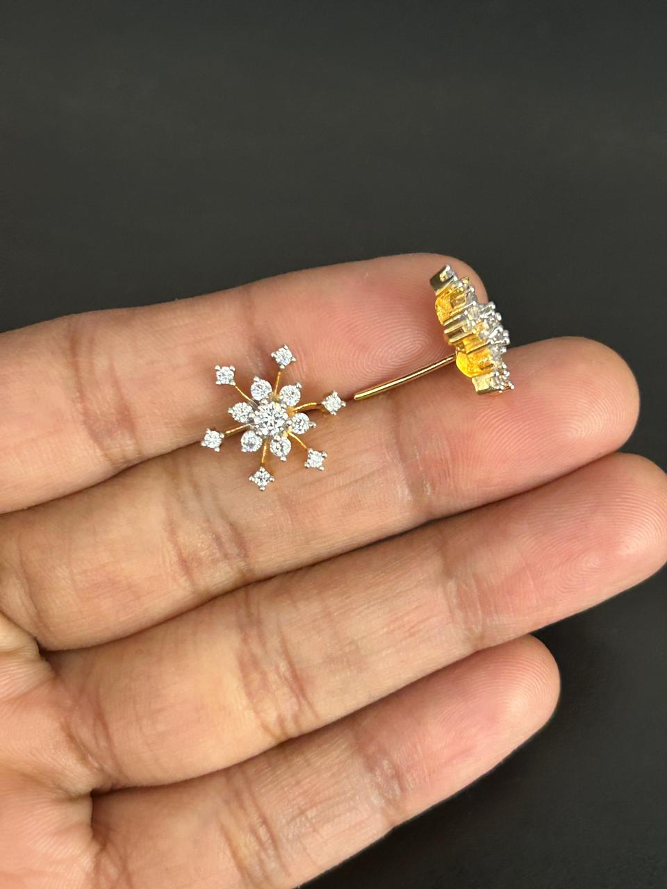 Two diamond earrings between fingers against a dark background