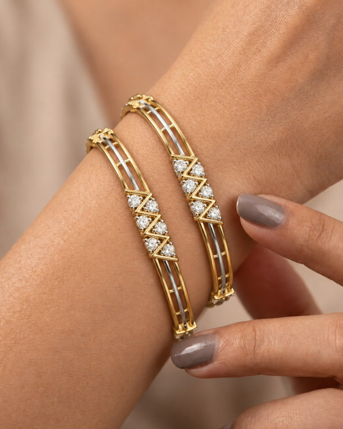 Two gold bangle bracelets with white enamel inlays and diamond accents, shown worn on a woman's wrist with her fingers gently touching one of the bracelets.