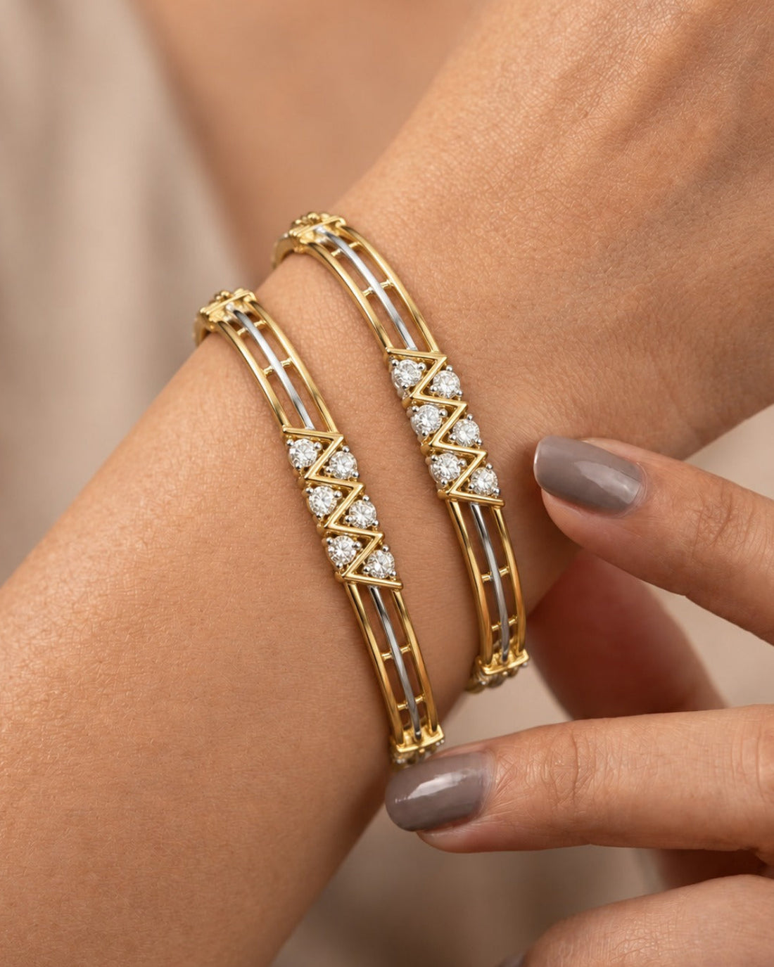 Two gold bangle bracelets with white enamel inlays and diamond accents, shown worn on a woman's wrist with her fingers gently touching one of the bracelets.