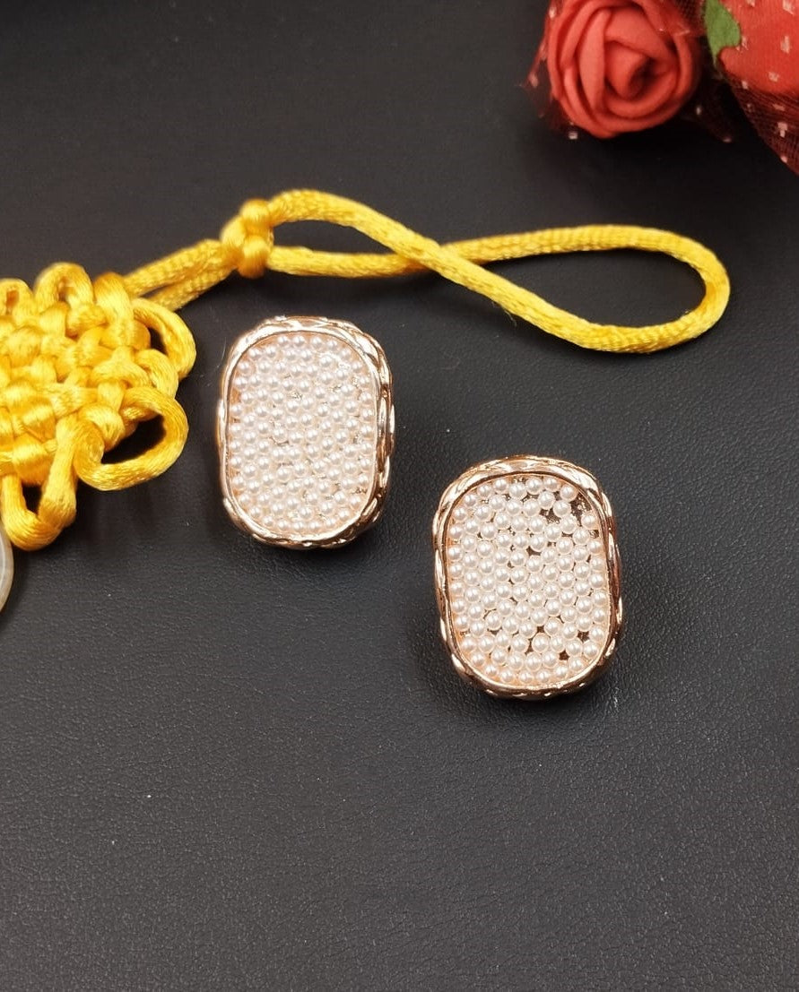 Two gold pendants on a black surface with a yellow string and red rose in the background.