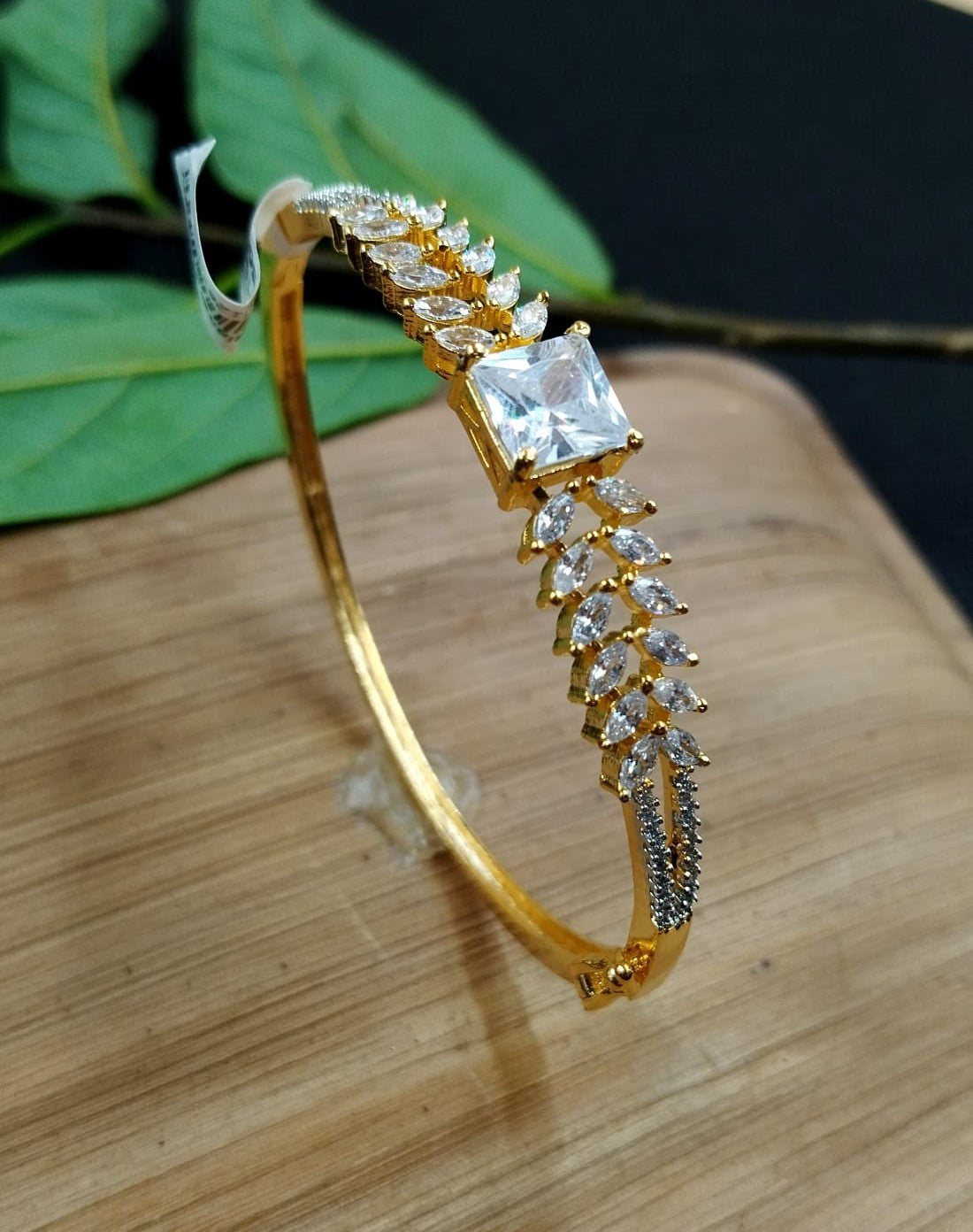 Gold bracelet with clear gemstones on a wooden surface with green leaves in the background
