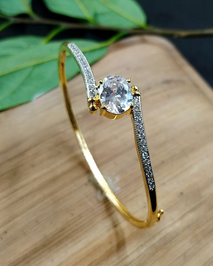 Gold bracelet with a central gemstone on a wooden surface