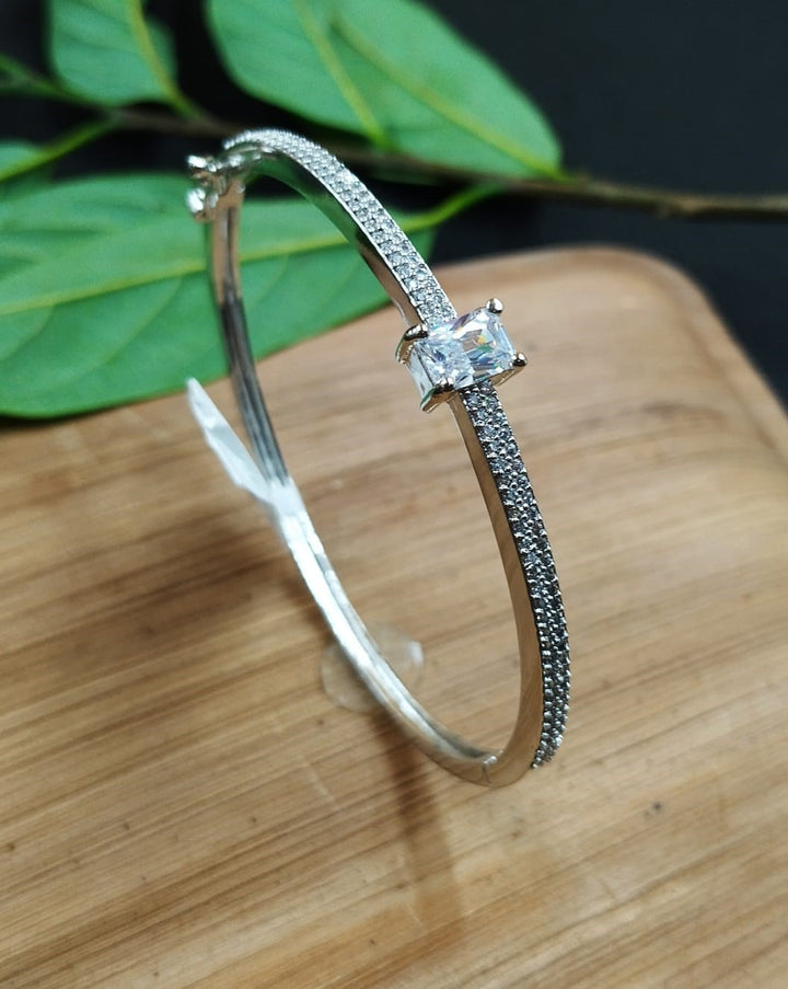 Silver bracelet with a central diamond on a wooden surface with green leaves in the background