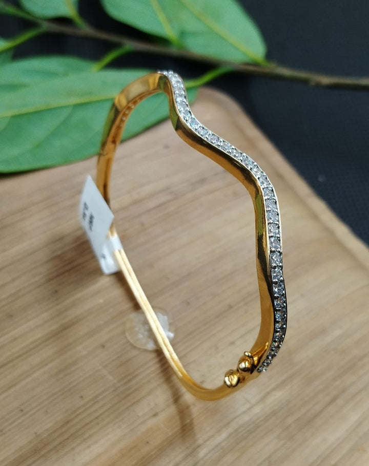 Gold bracelet with small stones on a wooden surface with green leaves in the background