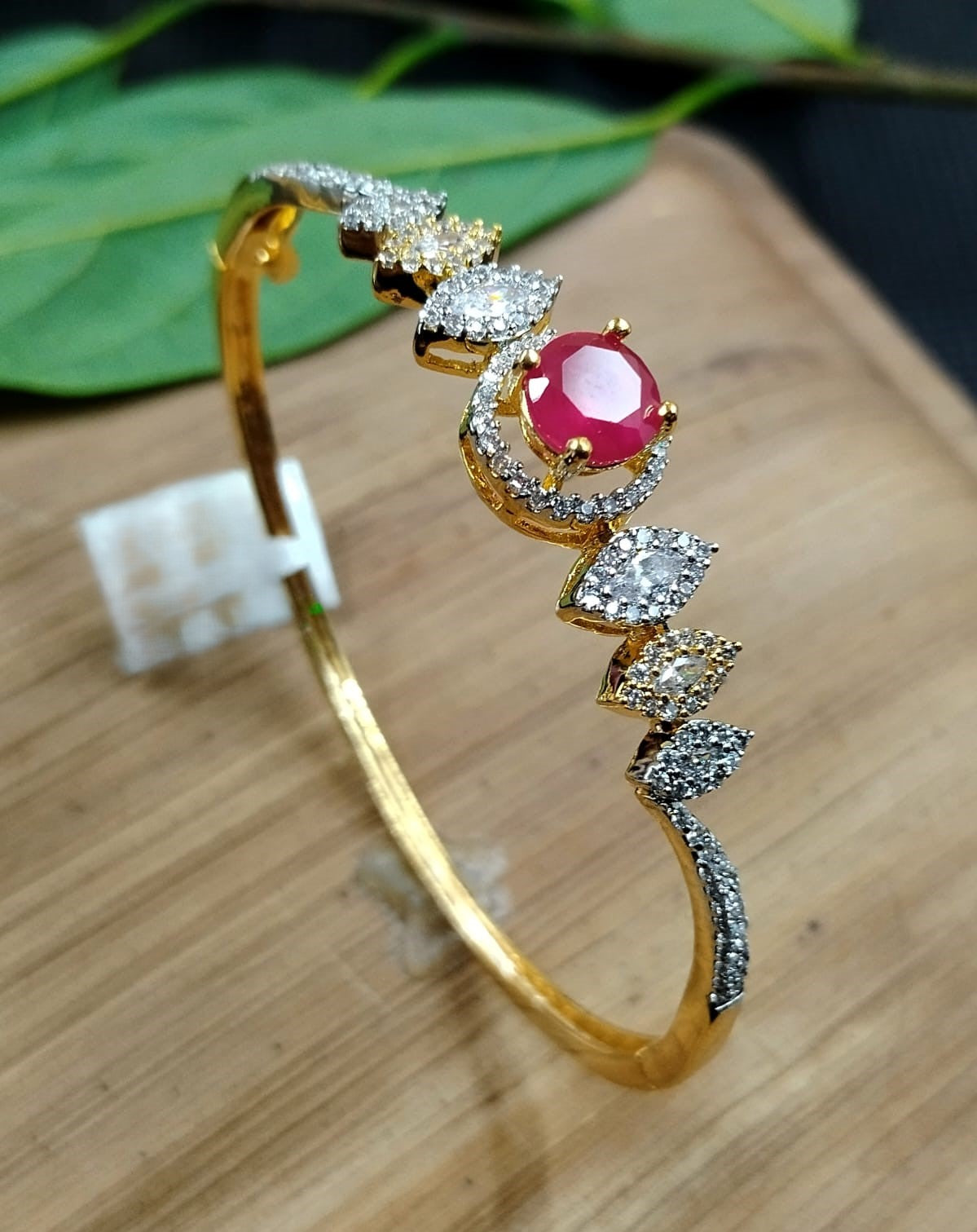 Gold bracelet with a red gemstone and diamonds on a wooden surface