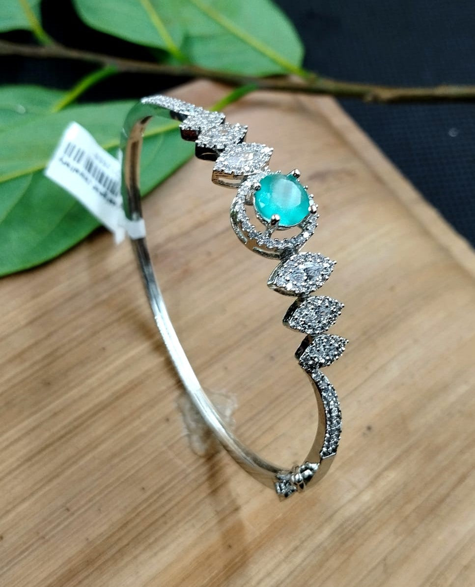 Silver bracelet with a turquoise gemstone on a wooden surface with leaves in the background