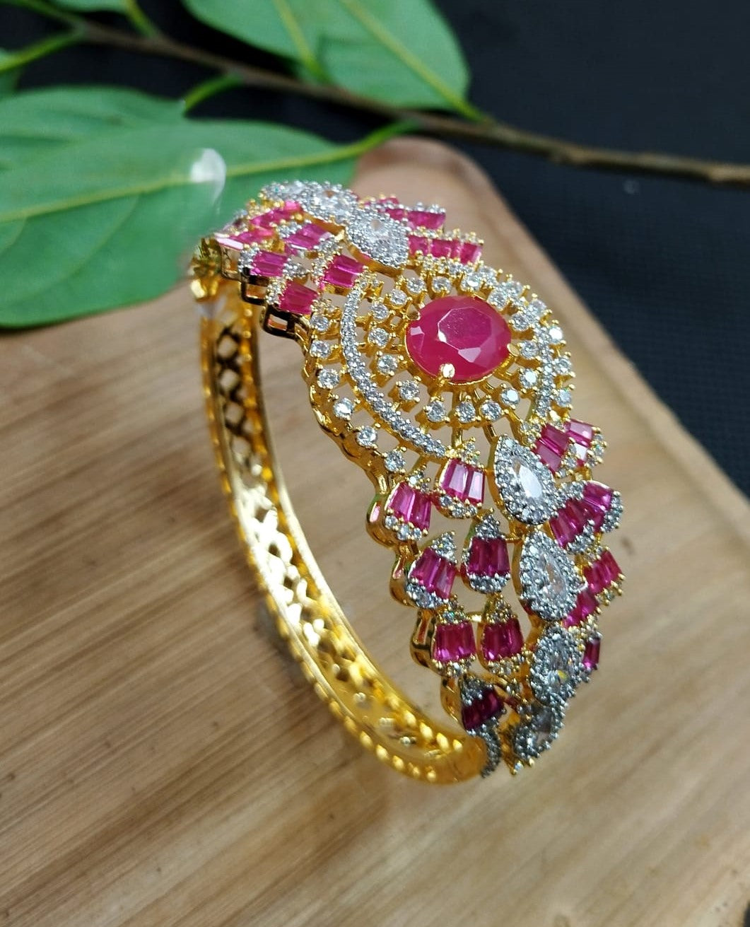 Decorative gold bangle with pink and white stones on a wooden surface