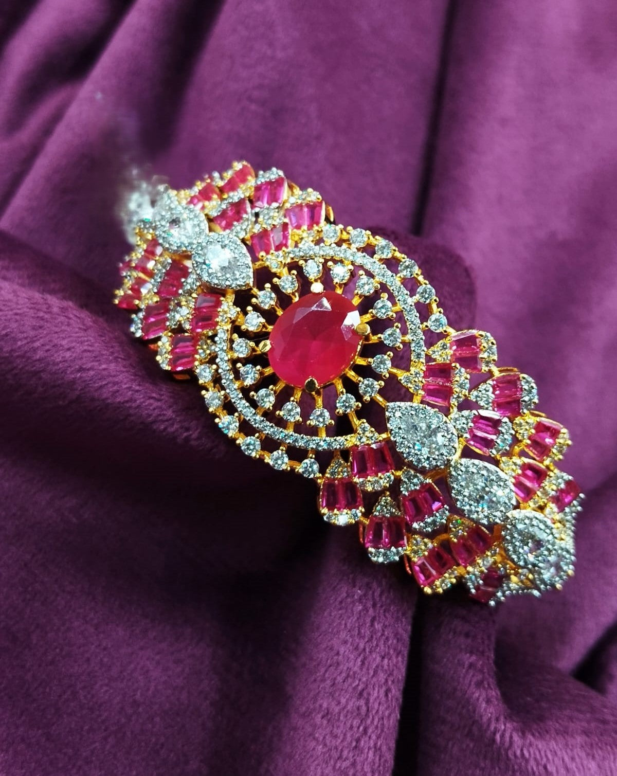 Decorative brooch with red gemstone and gold accents on a purple fabric background