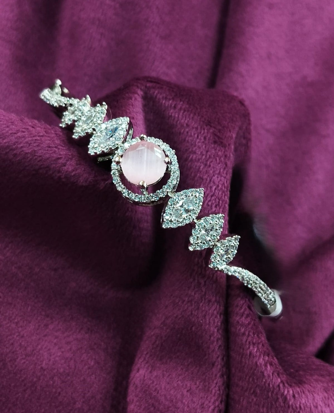 Silver earring with pink gemstone on a purple fabric background