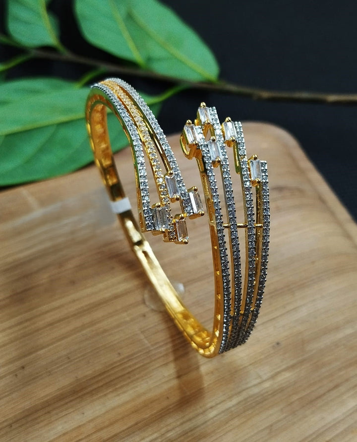 Gold bangles with diamond-like stones on a wooden surface with green leaves in the background