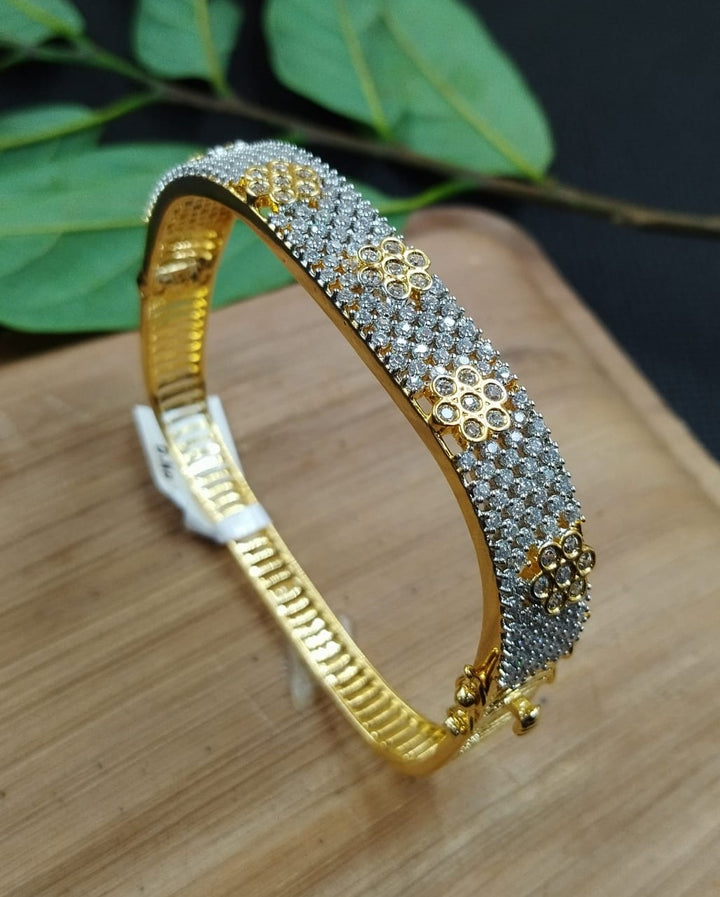 Gold and silver bracelet on a wooden surface with green leaves in the background