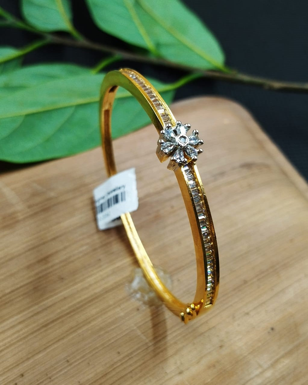 Gold bracelet with a diamond on a wooden surface with green leaves in the background