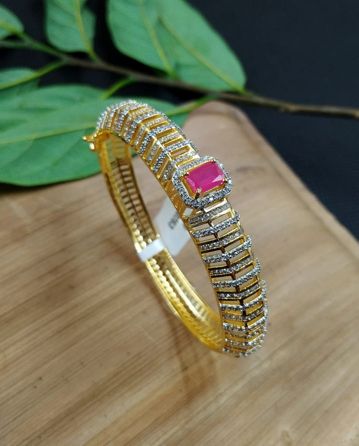 Gold bracelet with a pink gemstone on a wooden surface with green leaves in the background
