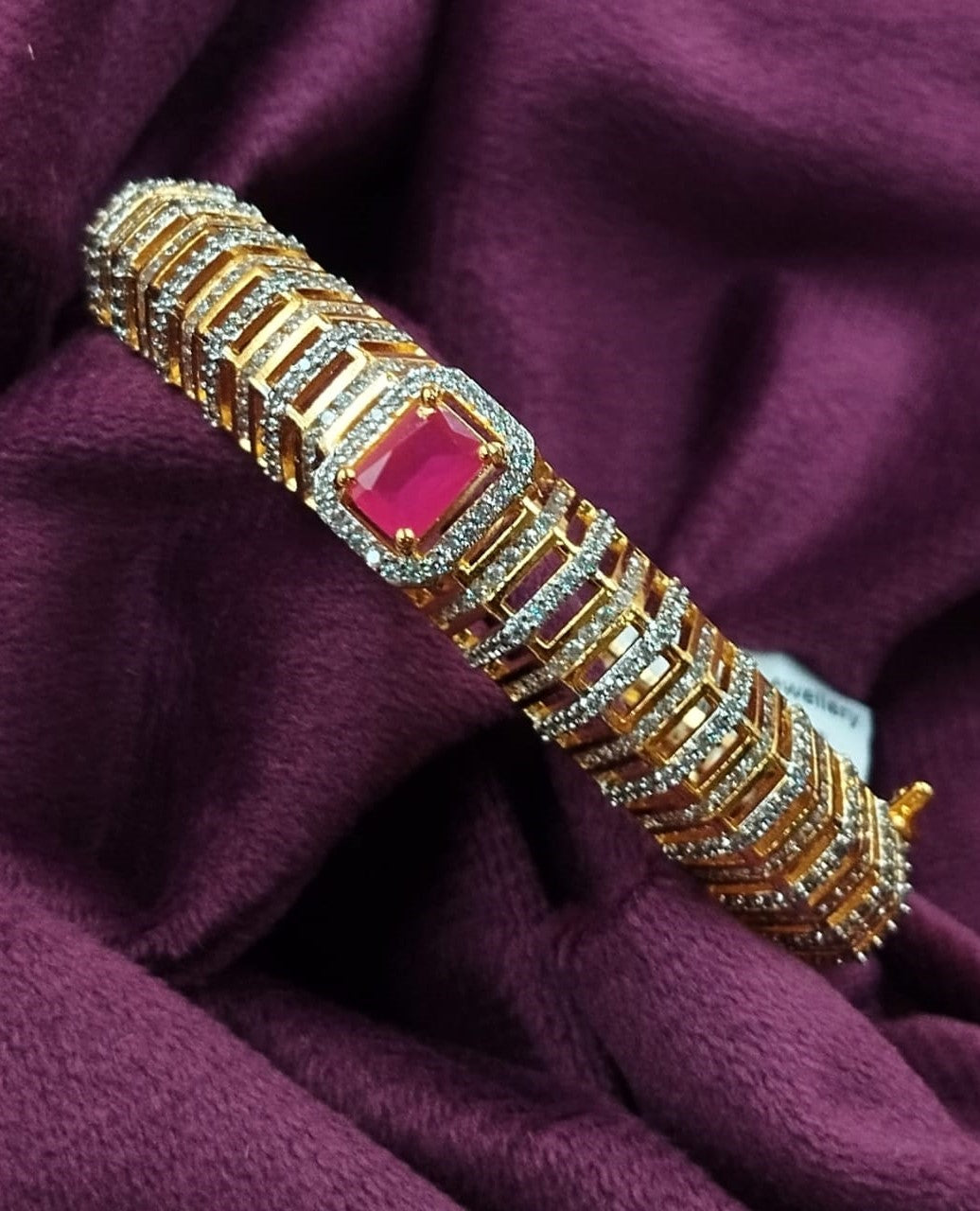 Gold bracelet with a red gemstone on a purple fabric background