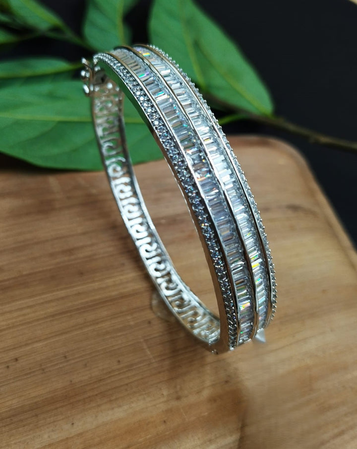 Silver bangles on a wooden surface with green leaves in the background