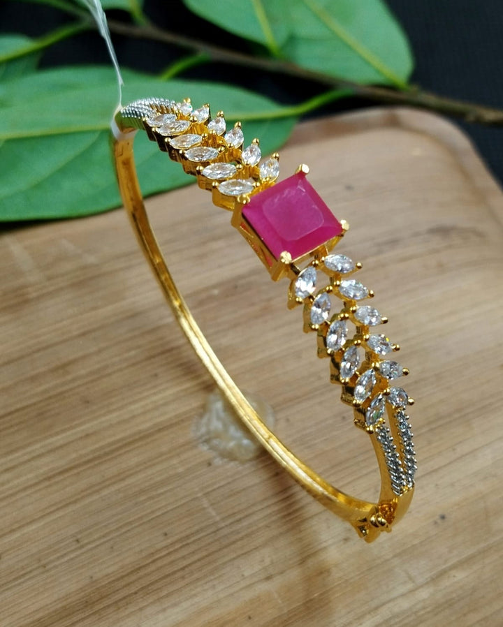 Gold bracelet with a pink gemstone on a wooden surface