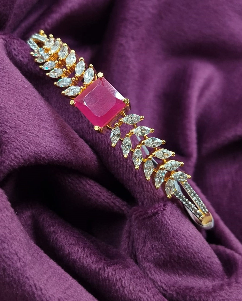 Jewelry brooch with pink gemstone and gold accents on a purple fabric background