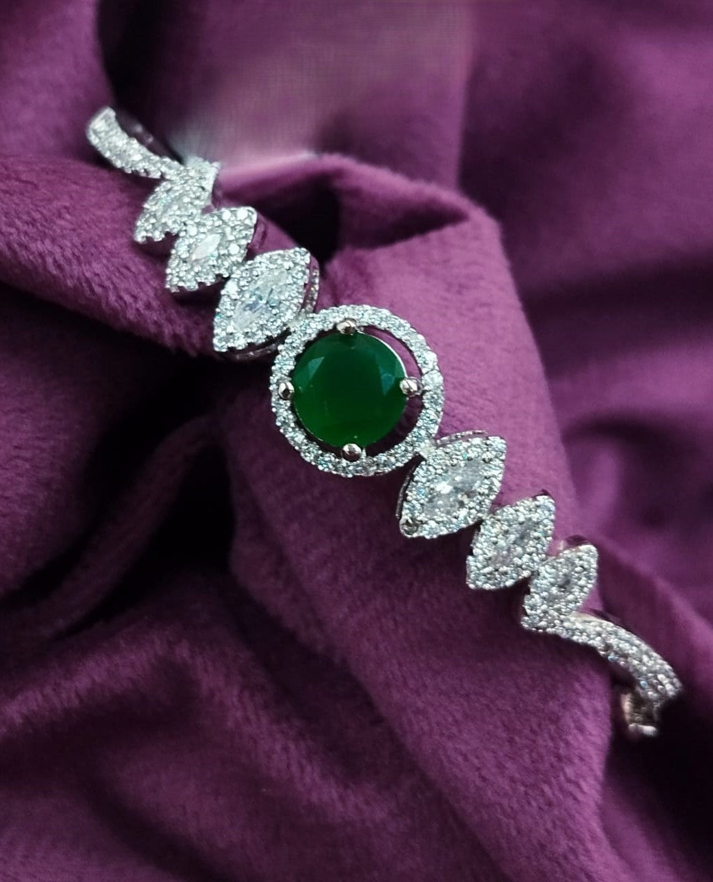Jewelry with a green gemstone and silver leaves on a purple fabric background