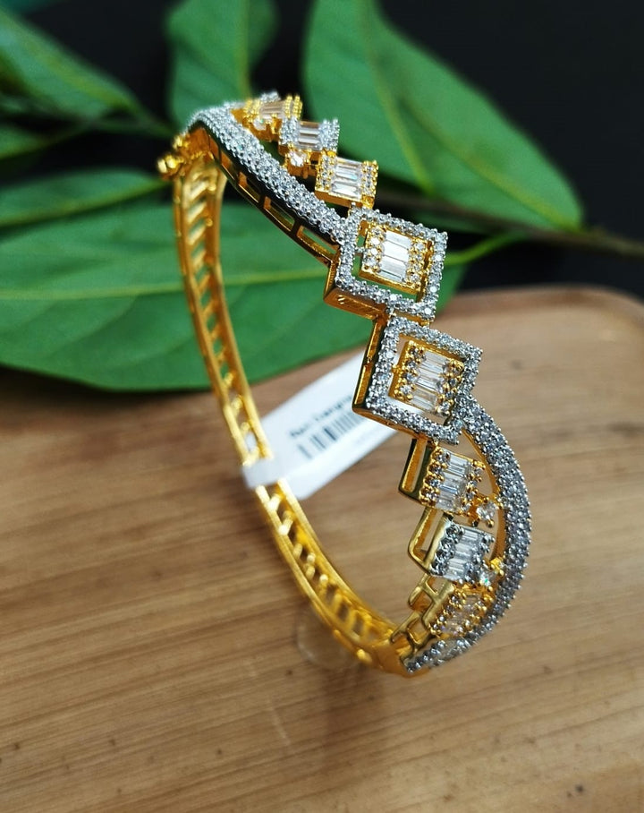 Gold bracelet with diamond accents on a wooden surface with green leaves in the background