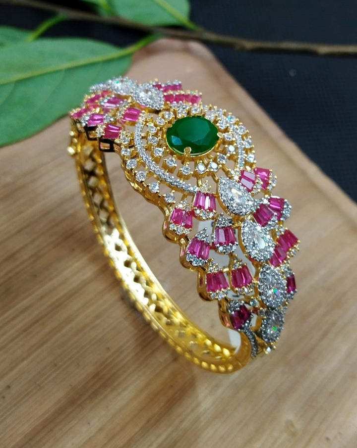 Gold bracelet with pink and green gemstones on a wooden surface