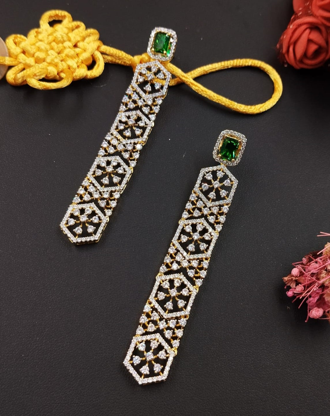 Decorative earrings with intricate patterns and green gemstones on a dark background.