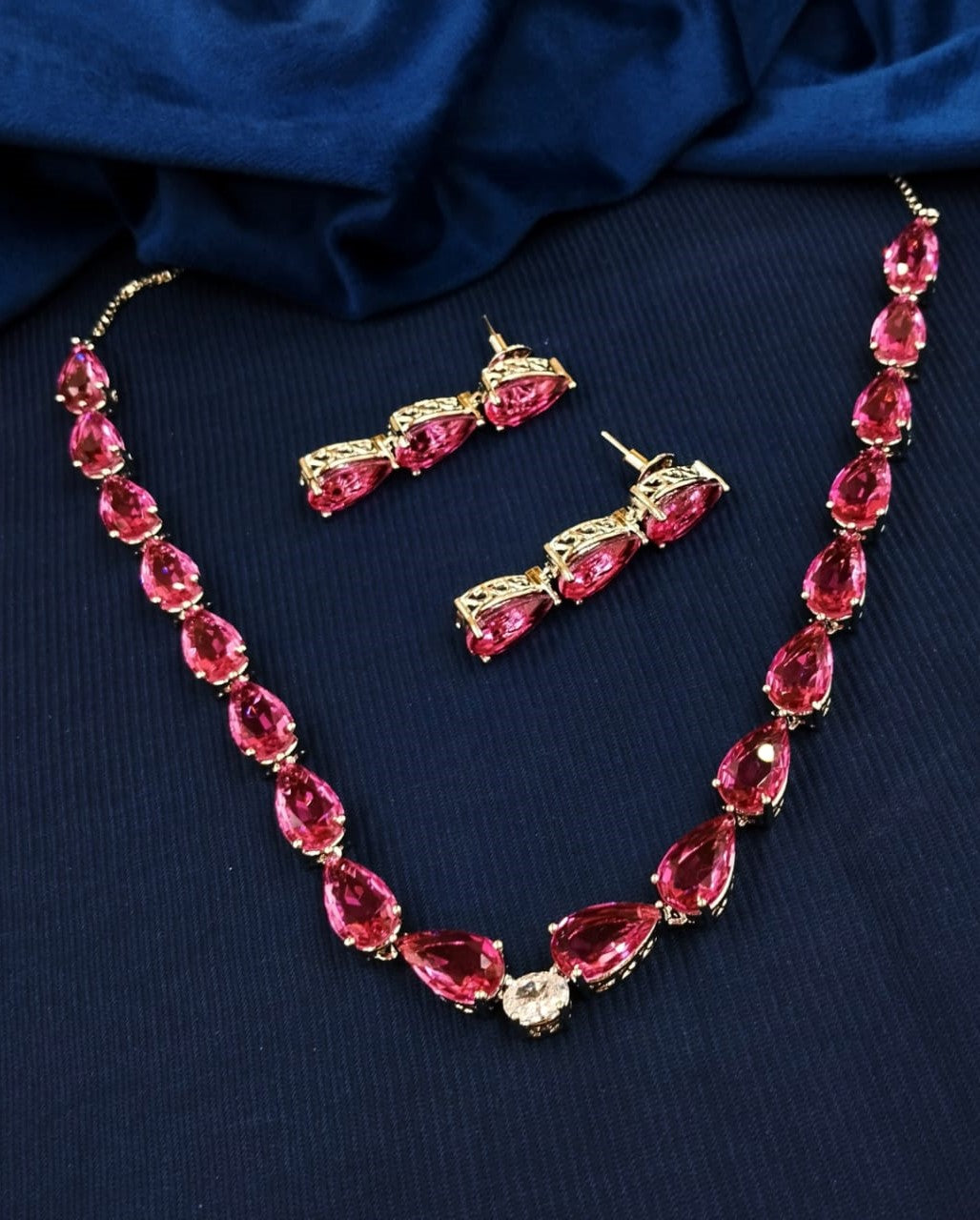 Jewelry set with pink gemstones and gold accents on a dark blue fabric background